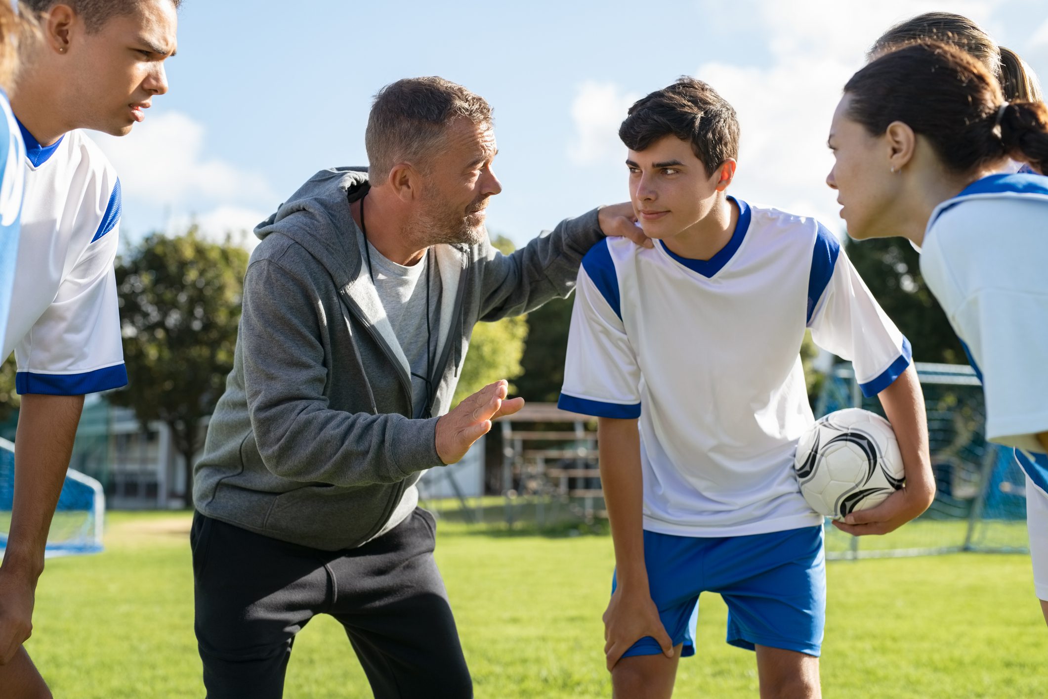Coach talking to young soccer team before the match Mature coach teaching strategy to high school team on football field. Young soccer players standing together united and listening coach motivational speech. Coach giving team advise before school match.